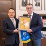 Na tle portretów dawnych dziekanów WFPiK stoi Dziekan Mizerkiewicz oraz gość z Chin, obaj trzymają chińską oprawioną grafikę przedstawiającą kwiaty i flagę Zhaoqing University.