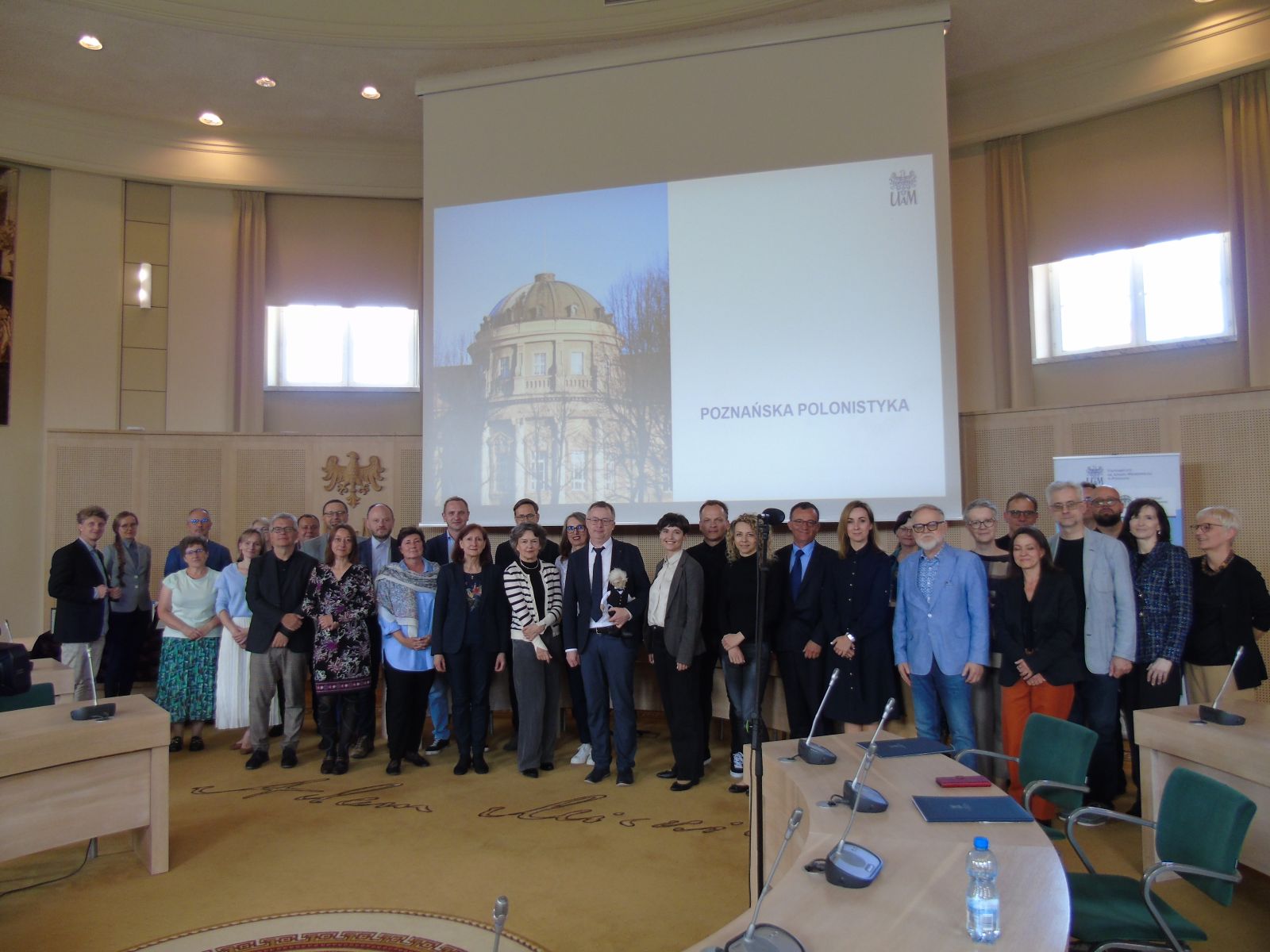 Zdjęcie grupowe uczestników Zjazdu w Salonie Mickiewicza na tle wyświetlanego na rzutniku zdjęcia Collegium Maius.