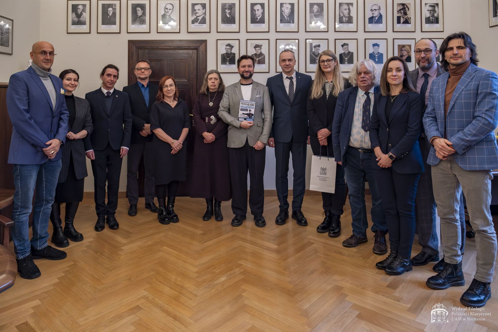 Wspólne zdjęcie w gabinecie dziekańskim na tle wiszących na ścianach portretów poprzednich dziekanów.