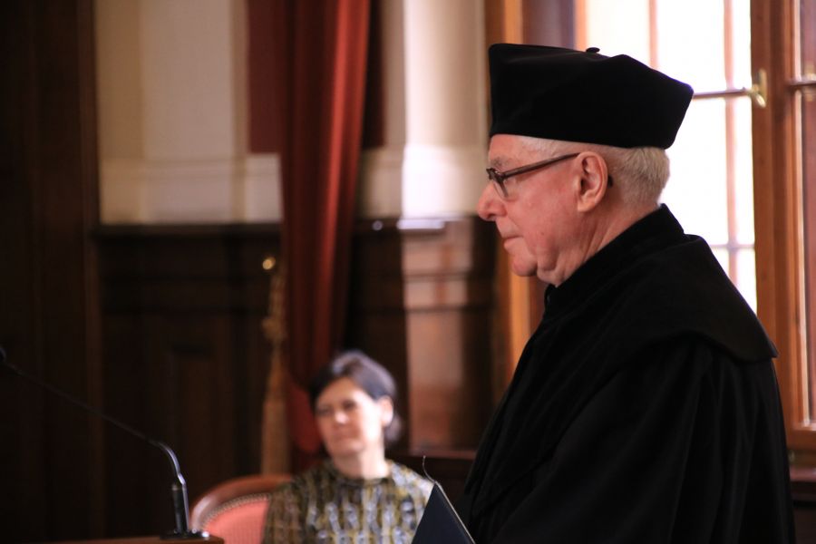 Prof. Danielewicz w czarnej todze i birecie stoi w Auli Lubrańskiego, zwrócony lewym profilem do obiektywu.