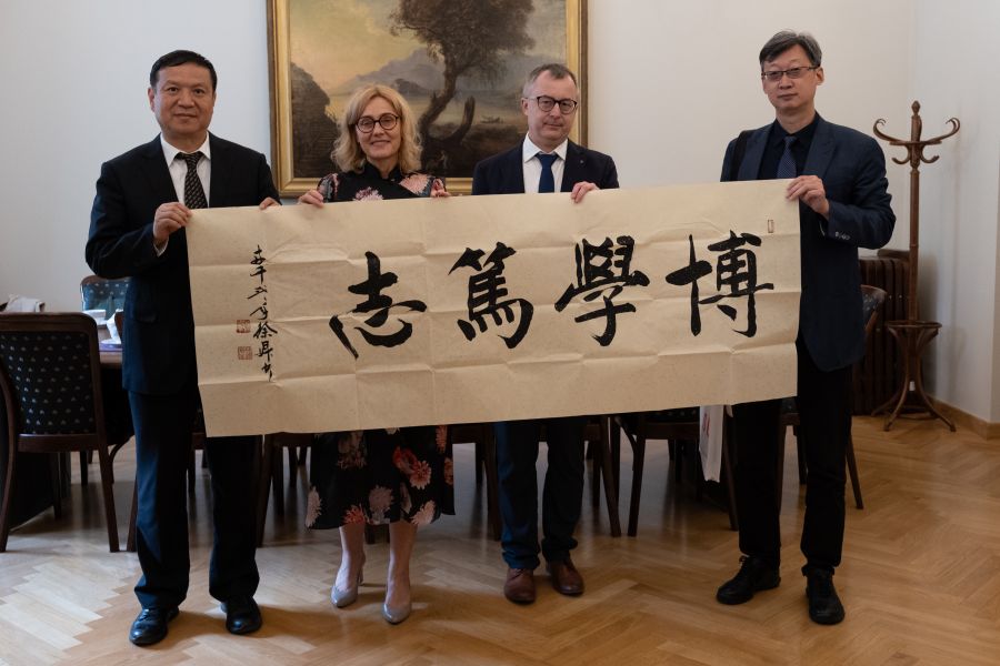 Cztery osoby - trzech mężczyzn stoją w gabinecie dziekana WFPiK, prezentując dużą papierową planszę z napisem w tradycyjnym alfabecie chińskim.