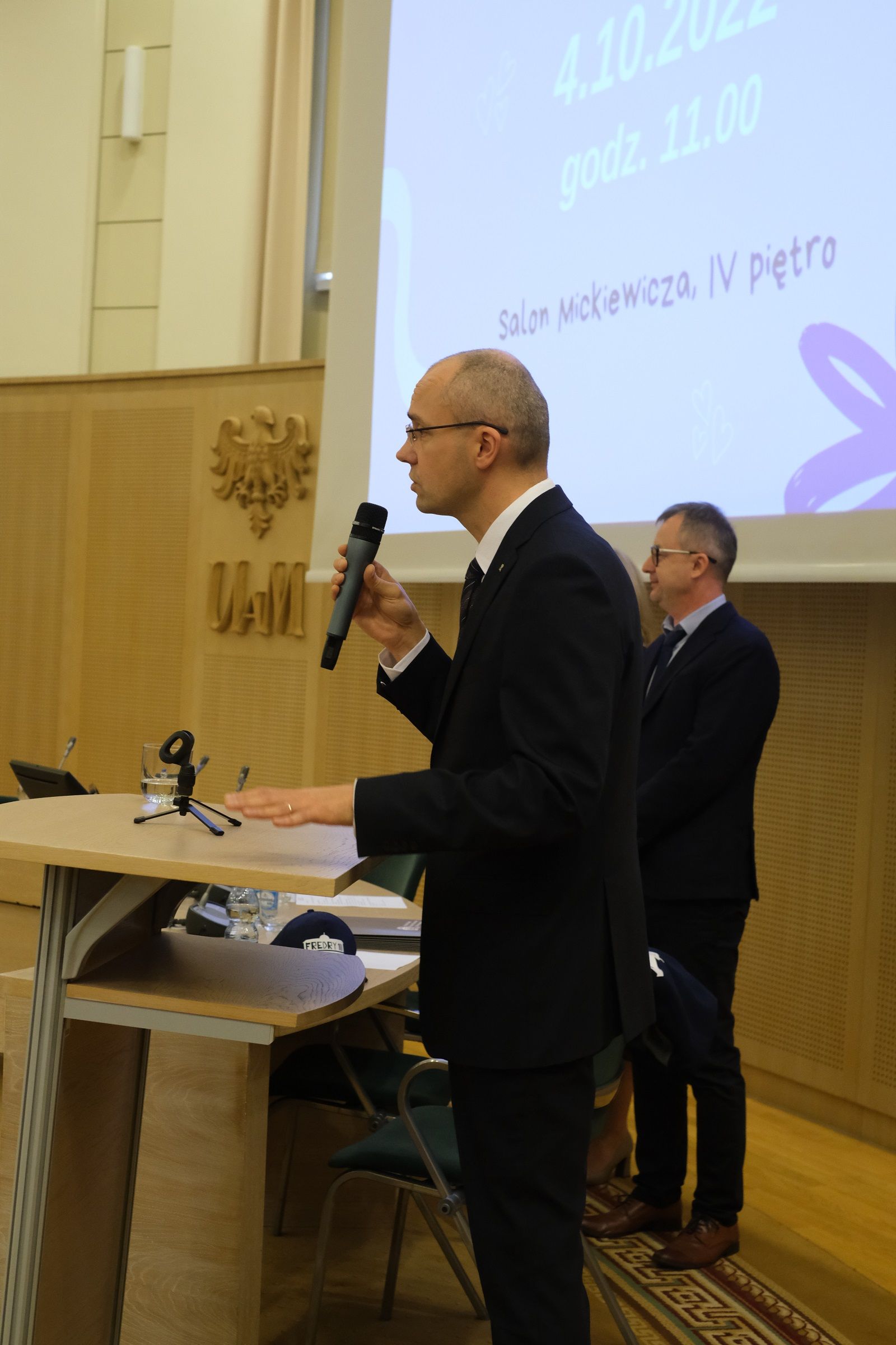 Prof. Krzysztof Skibski stoi przy mównicy i przemawia do mikrofonu, za nim stoi prof. Tomasz Mizerkiewicz.