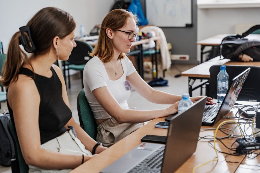 Dwie młode osoby siedzą przy laptopach, programując.