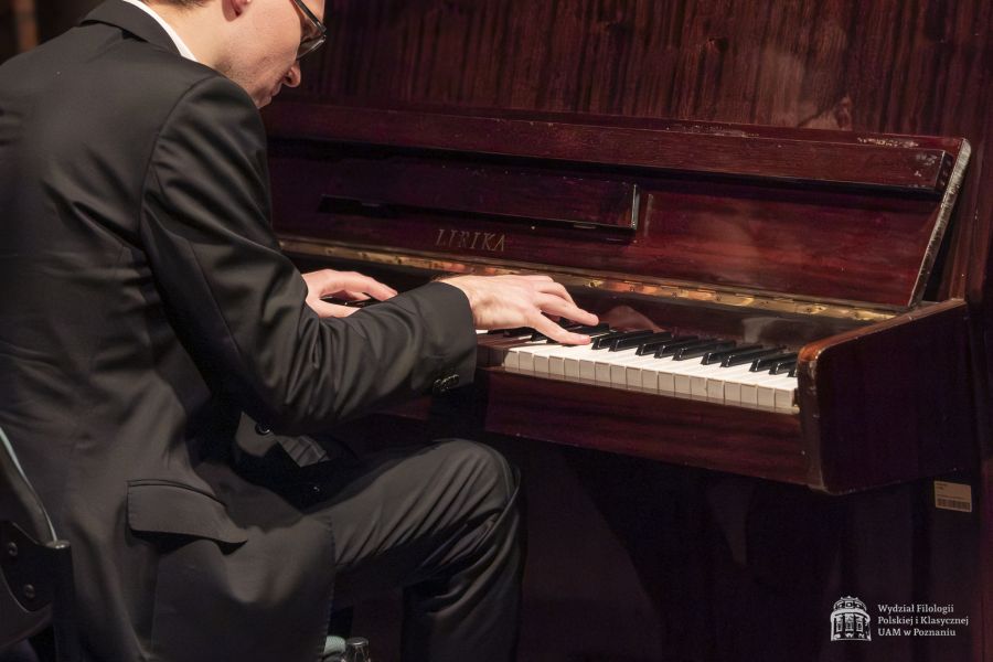 Miłosz Lewandowski wykonuje utwór na pianinie, pochylony nad klawiaturą.