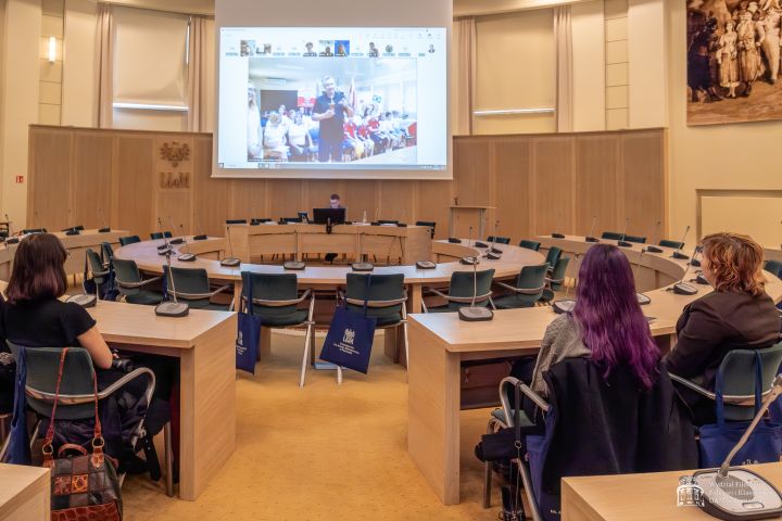 Uczestnicy wydarzenia łączący się poprzez MS Teams, wyświetleni na dużym ekranie w Salonie Mickiewicza.