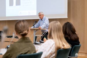 Prof. Connelly wygłasza wykład przy mównicy w Salonie Mickiewicza. Na pierwszym planie widać plecy kilku osób słuchających wykładu.