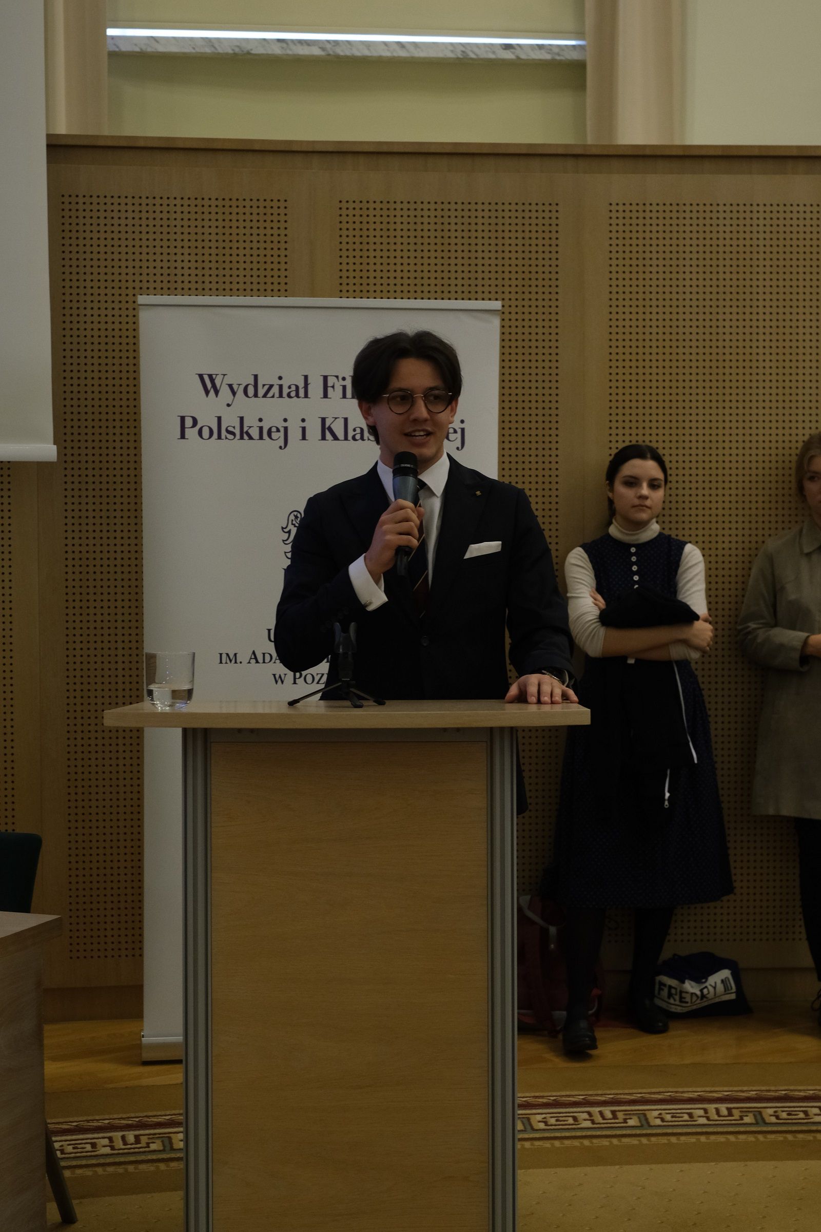 Przemysław Raczyk, Przewodniczący Rady Samorządu Studentów WFPiK, stoi przy mównicy i przemawia do mikrofonu.