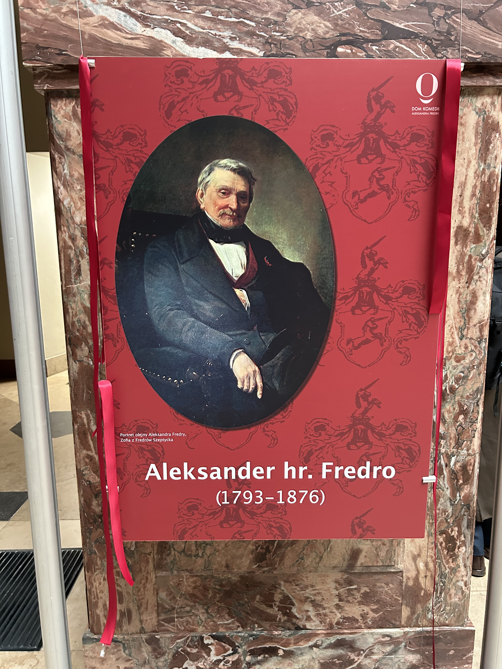 Tablica z portretem Aleksandra Fredry z przeciętąwstęgą.