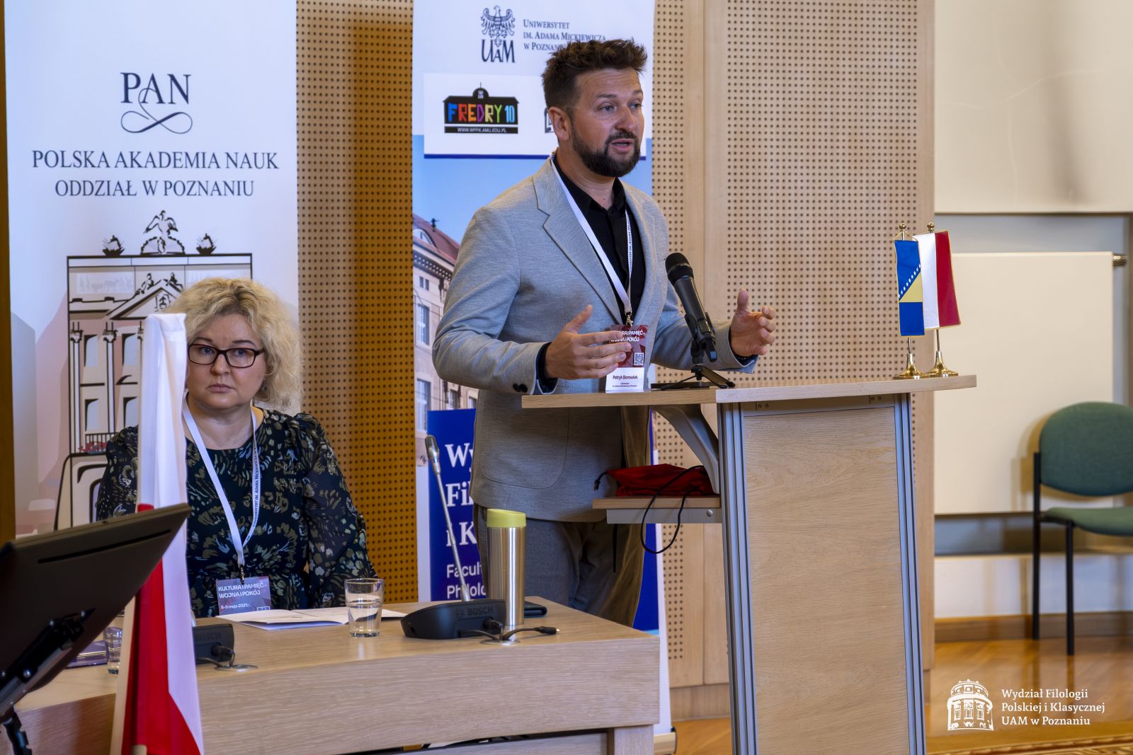 Dr hab. Patryk Borowiak przemawia przy mównicy, obok niego siedzi prof. Ewa Szperlik.
