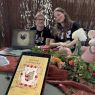 Dwoje studentów pozuje do zdjęcia siedząc za stoiskiem, na pierwszym planie widać tablet z aplikacją do tworzenia fantastycznych chowańców.