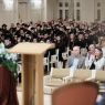 Uczestnicy absolutorium ubrani w togi i czapki absolwenckie siedzą w rzędach w Auli Uniwersyteckiej. 