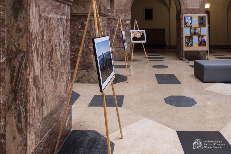 Wystawa zdjęć ustawiona na drewnianych sztalugach w holu Collegium Maius.
