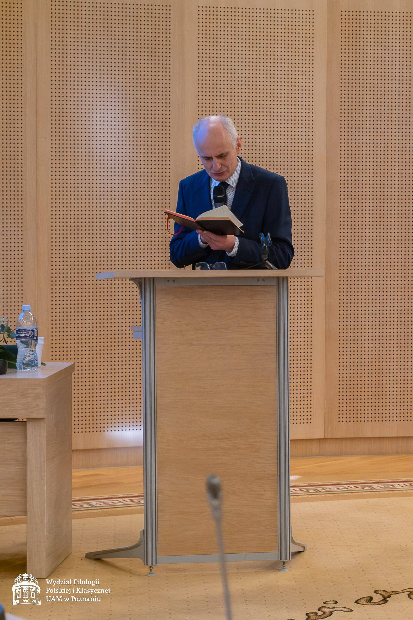 Przy mównicy stoi prof. Wiesław Ratajczak, czyta do mikrofonu coś z otwartej przed sobą książki.