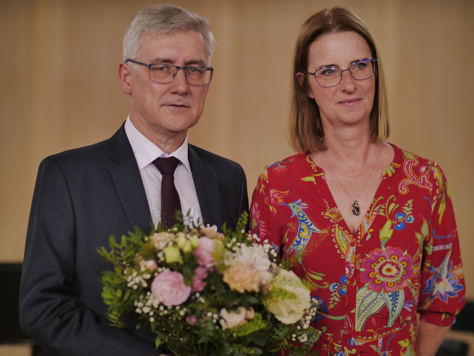 Prof. Jarosław Liberek pozuje do zdjęcia, trzymając bukiet kwiatów, obok niego stoi młoda kobieta w sukience.