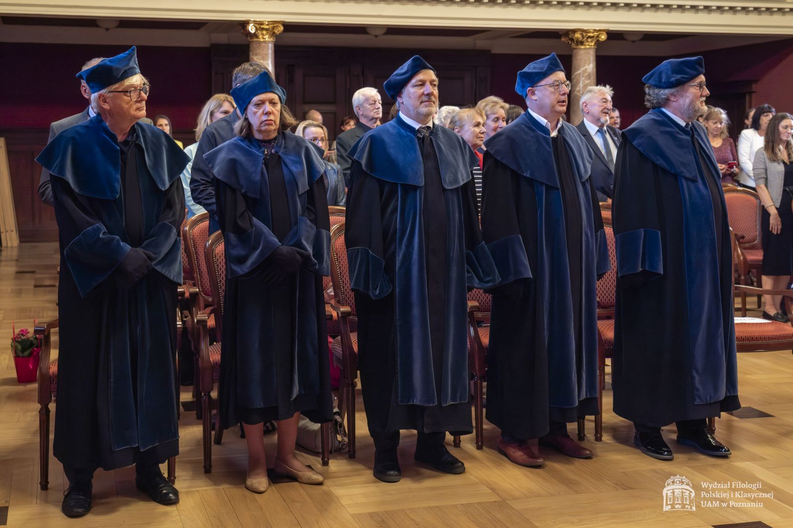 Promotorzy prac doktorskich stoją w niebieskich togach.