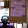 W holu głównym Collegium Maius stoi sztaluga z plakatami reklamującymi Dzień Studenta I roku, obok niej na stole pokrytym fioletowym suknem siedzi pacynka Aleksandra Fredry.