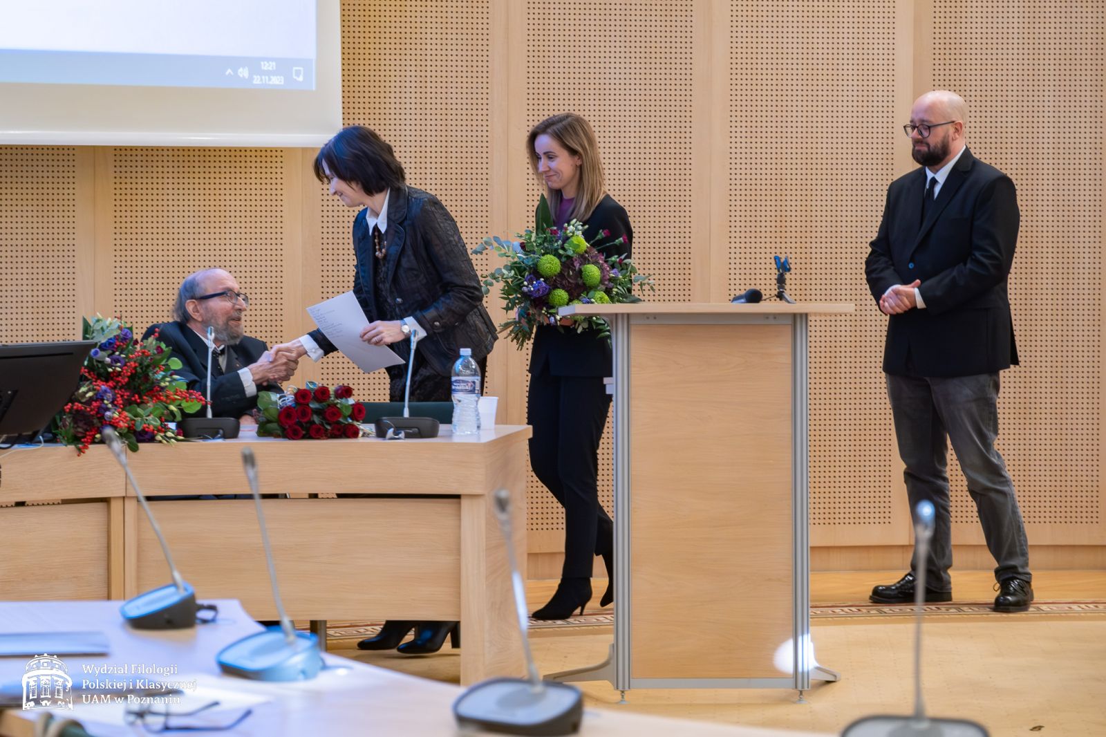 Dyrekcja IFP składa życzenia jubilatowi - prof. Elżbieta Winiecka ściska dłon prof. Lewandowskiemu, za nią dr Sylwia Karolak z bukietem kwiatów w rękach, jeszcze dalej prof. Marek Osiewicz.