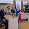Prof. Ewa Szperlik przemawia przy mównicy, obok niej za stołem prezydialnym siedzą: dyrektorka Teatru im. Fredry w Gnieźnie Joanna Nowak, prof. Sanjin Kodrić, dr hab. Patryk Borowiak, prof. UAM dr hab. Krzysztof Skibski. Przed stołem prezydialnym ustawiono flagę Polski i Bośni i Hercegowiny.