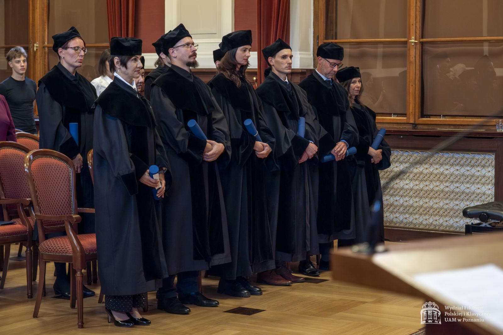 Doktoranci w togach stoją w Auli Lubrańskiego.