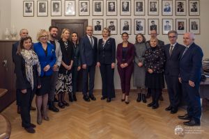 Goście WFPiK wraz z zespołem dziekańskim i pracownikami IFS pozują do wspólnego zdjęcia na tle ściany z fotografiami poprzednich dziekanów Wydziału.